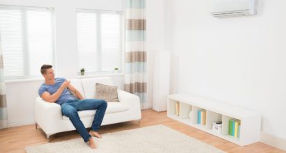 44592155 - young man on sofa operating air conditioner with remote control